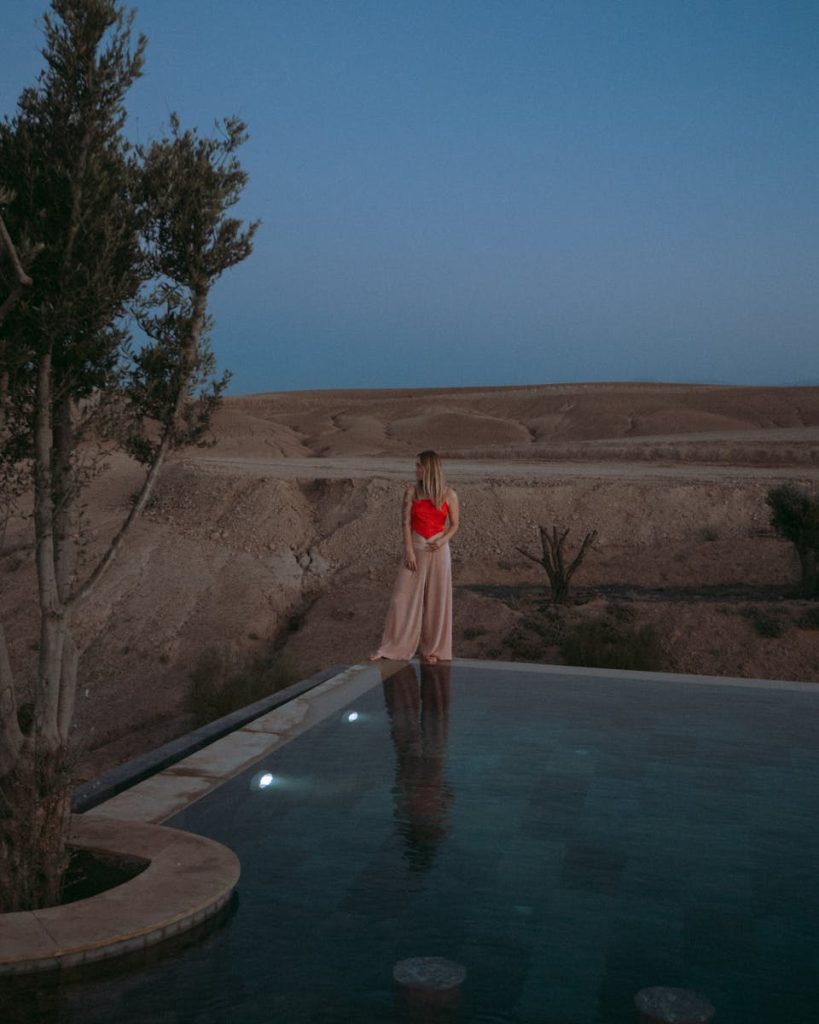 A woman in a vibrant dress standing by an infinity pool in the Agafay Desert, Morocco.