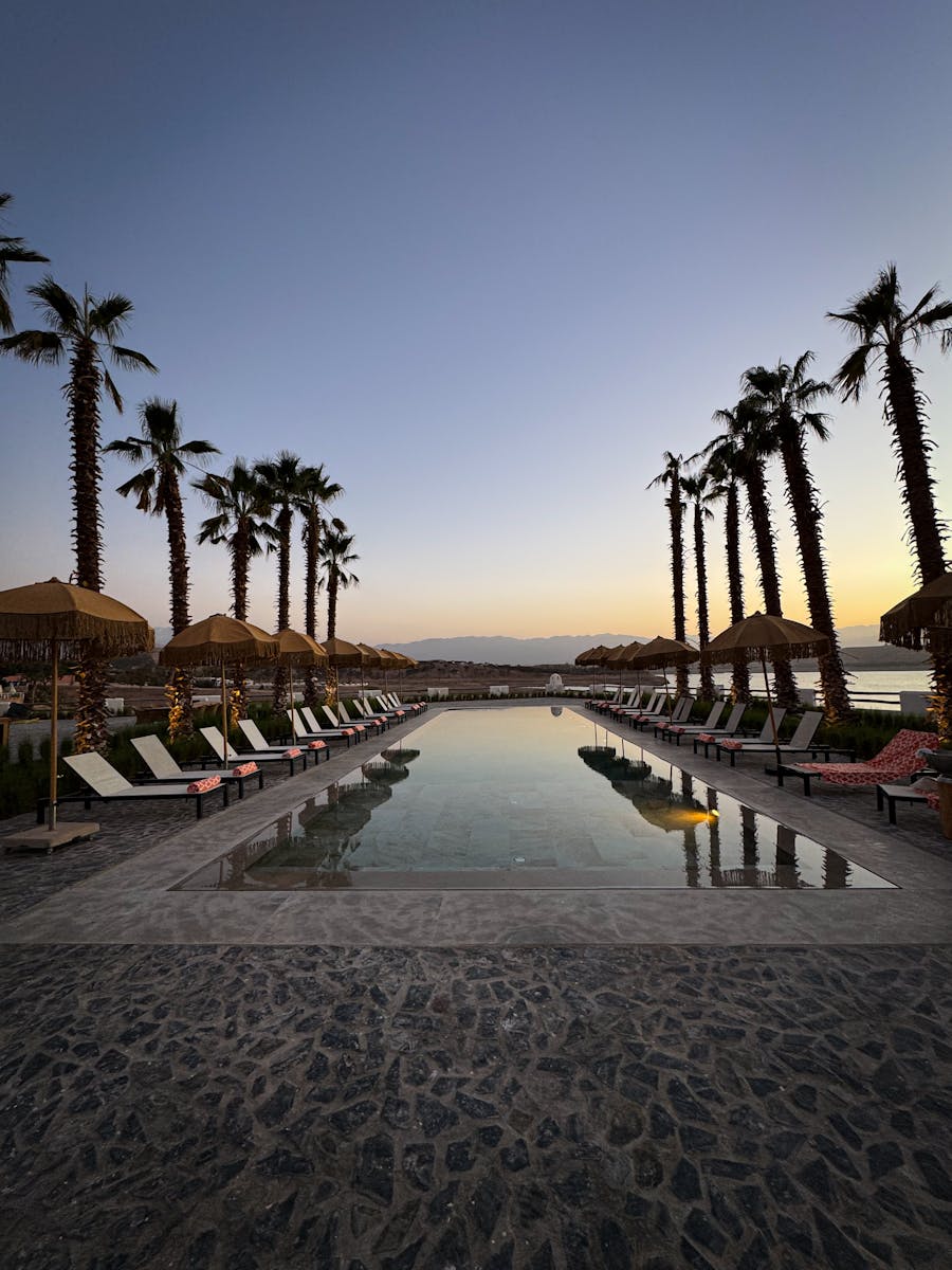 Tranquil poolside at sunset in Aguergour, surrounded by palm trees against the Moroccan desert backdrop.