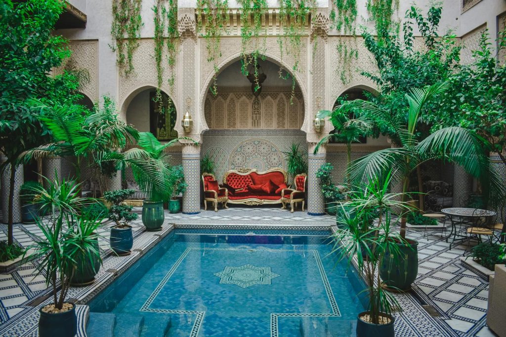 Elegant Moroccan courtyard featuring lush greenery and a decorative pool, perfect for a serene escape.